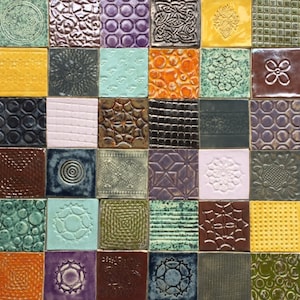 Peut inclure: Une mosaïque de 36 carreaux de céramique carrés de différentes couleurs et textures. Les carreaux présentent des motifs en relief, notamment des motifs floraux, géométriques et abstraits. Les couleurs varient du jaune et de l'orange au bleu, vert et violet.