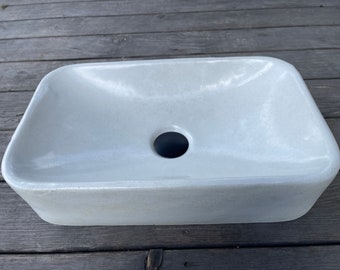 May include: A white rectangular concrete vessel sink with a round drain hole.