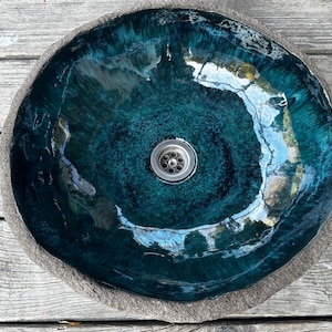 May include: A teal blue ceramic sink with a round shape and a drain in the center. The sink is set on a wooden surface.