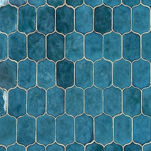 May include: A close-up of a blue tiled wall with a pattern of interlocking ovals. The tiles have a slightly textured surface and are outlined in a thin, gold-colored grout.