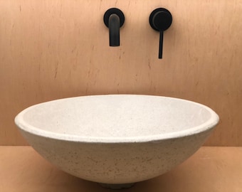 May include: A white concrete vessel sink with a rounded, bowl-shaped design. The sink is mounted on a wall with black faucet fixtures.