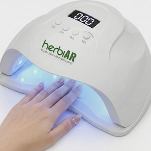 May include: A white nail lamp with a digital display showing "000" and buttons for 10s, 30s, 60s, and 99s settings. The lamp has the text "herbiAR Super Sunuvled Nail Lamp" and a hand with manicured nails is placed inside the lamp.