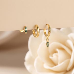 May include: A set of three gold-toned earrings consisting of one stud earring with a marquise-cut green moss agate stone, one plain gold hoop earring, and one gold hoop earring featuring a dangling marquise-cut green moss agate stone charm.