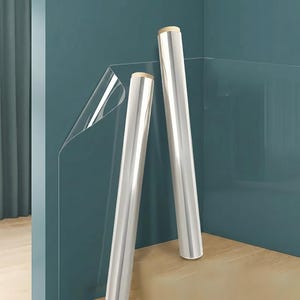May include: Two rolls of clear, transparent protective film with light brown cardboard cores. The film is partially unrolled, revealing a smooth, glossy, and flexible plastic surface that is completely see-through and reflects light.