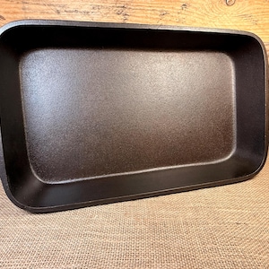 May include: A rectangular, dark brown cast iron baking pan with integrated handles. The pan has a slightly textured surface and is designed for even heat distribution. Ideal for baking casseroles, roasting vegetables, or making desserts.