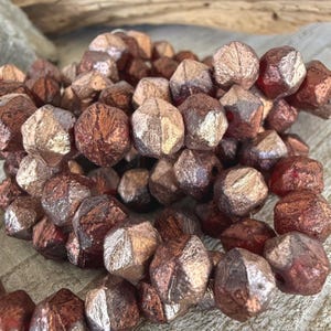 May include: Strand of faceted beads in shades of copper and bronze. The beads have a geometric shape with multiple facets, creating a textured and reflective surface. The beads are strung together, suggesting they are for jewelry making or crafting.