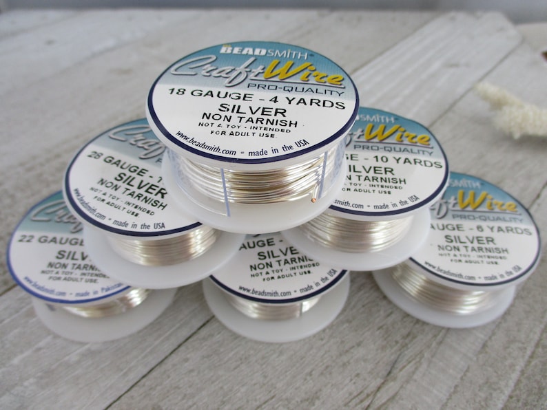 May include: A stack of silver craft wire spools. Each spool is labeled with gauge, yardage, and the words "Silver Non Tarnish." The labels also include the brand name "BeadSmith Craft Wire."