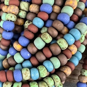 These 5/0 (about 4.5mm) are a blend of matted blues, greens and red browns with a light picasso finish that gets partially removed in the matting process.