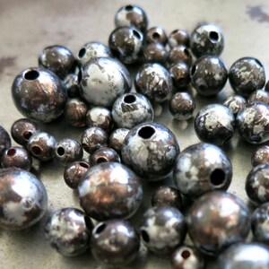 May include: A close-up of a pile of silver and black beads. The beads are round and have a speckled finish.