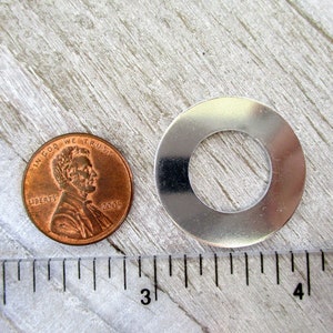 May include: A silver metal washer with a hole in the center, next to a US penny, measured with a ruler. The washer is approximately 1 inch in diameter.