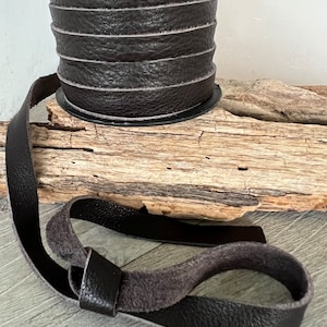 May include: A roll of dark brown leather cord with a length of cord tied in a knot. The cord is on a wooden surface.