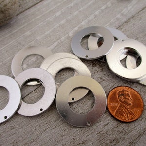 May include: A group of silver metal washers with a hole in the center. The washers are arranged in a circle around a penny.