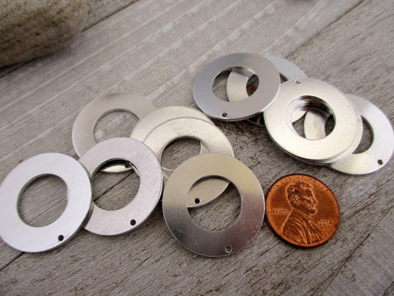 May include: A group of silver metal washers with a hole in the center. The washers are arranged in a circle around a penny.