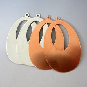 May include: Three oval-shaped metal earring blanks, two are copper and one is silver. The blanks have a hole at the top for attaching earring hooks.