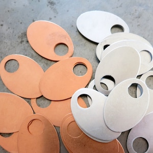 May include: A pile of oval-shaped metal tags with a hole in the centre. Some tags are copper coloured and some are silver coloured.
