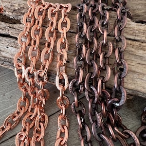 May include: Two strands of copper chain with an ornate design. The chain on the left is a lighter copper color, while the chain on the right is a darker copper color.