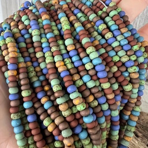 Pode incluir: Fios de contas coloridas em tons de castanho, azul, verde e amarelo. As contas s&atilde;o pequenas e redondas, com um acabamento mate. As contas s&atilde;o enfiadas, criando um efeito texturizado e em camadas. As contas s&atilde;o provavelmente para fazer joias.
