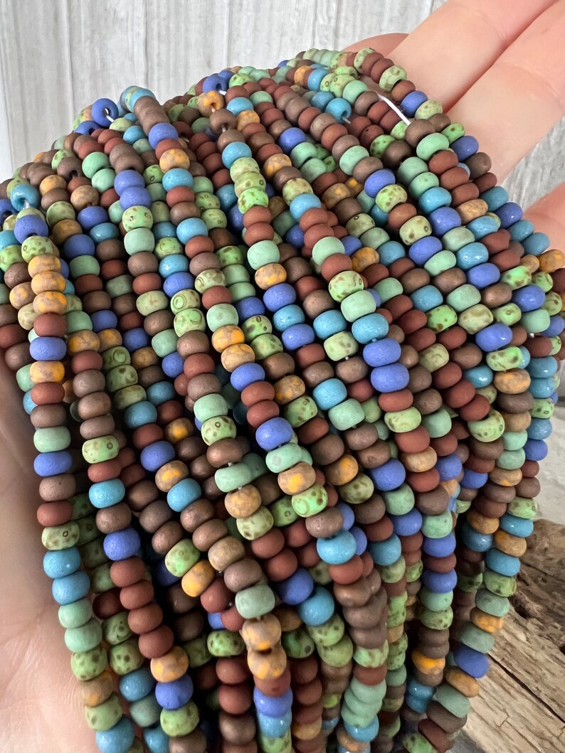 Pode incluir: Fios de contas coloridas em tons de castanho, azul, verde e amarelo. As contas s&atilde;o pequenas e redondas, com um acabamento mate. As contas s&atilde;o enfiadas, criando um efeito texturizado e em camadas. As contas s&atilde;o provavelmente para fazer joias.