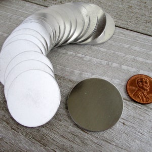May include: A stack of 20 silver metal round discs, each about the size of a UK penny, with one disc laying flat next to the stack.