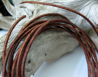 May include: Close-up of several strands of brown leather cord, tightly coiled and arranged against a light-colored, textured wooden surface. The cord has a slightly rough texture and a rich, warm brown color, suggesting a natural material.