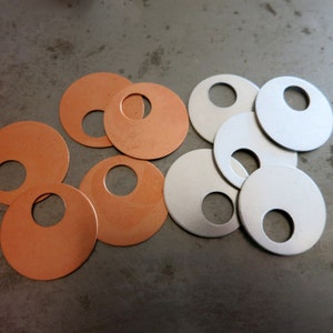 May include: A group of copper and silver metal washers with a hole in the centre. The washers are arranged in a semi-circular pattern.