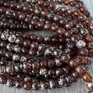 May include: A strand of brown glass beads with a speckled silver finish. The beads are round and have a slightly irregular shape.
