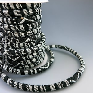 May include: A spool of black and white patterned trim. The trim is wound around a white spool and a length of the trim is draped over the spool.
