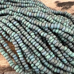 Peut inclure: Un brin de perles de verre bleu sarcelle et gris. Les perles sont petites et rondes, et elles ont une finition mate.
