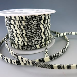 May include: A spool of black and white striped cord or trim. The cord is wound around a white plastic spool.