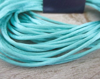 May include: A close-up of a spool of light blue embroidery floss.