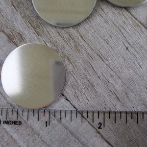 May include: A silver metal disc measuring 1 inch in diameter. The disc is smooth and reflective, and it is sitting on a wooden surface.