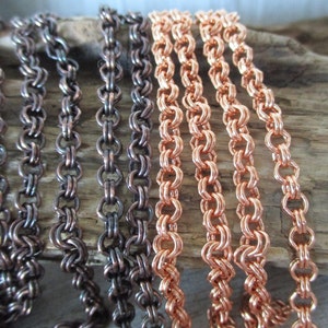 May include: Close-up of two different types of chain, one in copper and one in a dark metal. The chains are laid out side-by-side on a piece of driftwood.