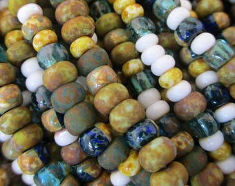 May include: Close-up of a variety of glass beads in shades of green, blue, yellow, and white. The beads are arranged in rows and are all approximately the same size.