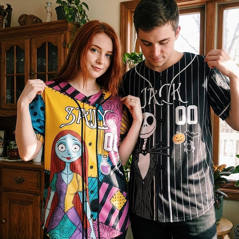 Op de afbeelding: Twee honkbalshirts. E&eacute;n is geel, blauw en roze met een Sally-gezicht en de naam "SALLY". De andere is zwart en wit gestreept met "JACK" en een Jack Skellington-afbeelding.