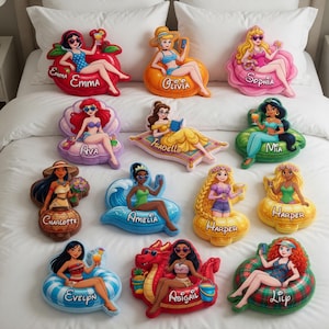 May include: A collection of colorful, decorative pillows shaped like various characters, each lounging on a unique floatation device. Each pillow features a character's name, such as "Emma", "Olivia", and "Sophia". The pillows are arranged on a white bed.
