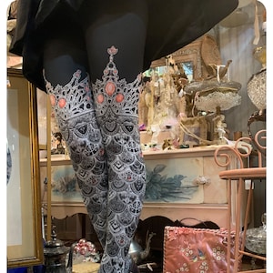 May include: Black tights with a white and silver crown design and red jewels. The tights are worn by a person with black boots.