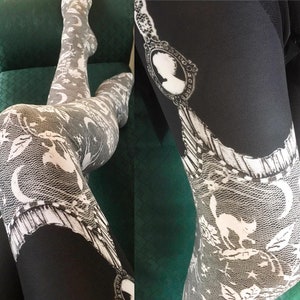 May include: Black leggings with a white lace pattern featuring a crescent moon, stars, and a silhouette of a cat.