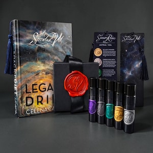 Peut inclure: Ensemble d'articles comprenant un livre intitulé "The Stardust Veil", une boîte cadeau noire scellée avec de la cire rouge et plusieurs flacons de parfum. Le livre a un pompon bleu, et les flacons ont des étiquettes colorées.