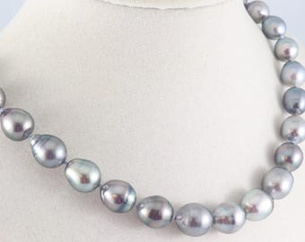 Op de afbeelding: Een ketting bestaande uit talloze grijze, barokvormige parels. De parels vertonen een glanzende, metallic glans met subtiele kleurnuances, variërend van lichtzilver tot diep antraciet, aaneengeregen in een enkele streng rond de hals.