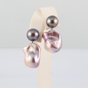 May include: A pair of pearl earrings. Each earring features a dark gray, round pearl stud, connected to a large, iridescent, baroque pearl. The baroque pearls have a pink and lavender hue, with a unique, irregular shape.
