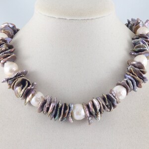 Op de afbeelding: Een ketting gemaakt van iriserende, veelkleurige barokparels met een witte parel als accent. De parels zijn geregen aan een zilveren ketting.