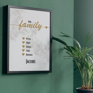 Könnte beinhalten: Gerahmter Familien-Kunstdruck mit dem goldenen Schriftzug "Our family". Darunter sind Namen mit Herzsymbolen aufgelistet. Der Familienname "Jacobs" ist unten fett gedruckt. Der Druck befindet sich in einem schwarzen Rahmen.