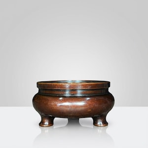 May include: A brown, three-legged incense burner with a rounded body and a wide rim. The burner has a glossy finish and a dark band around the middle. The design is simple and elegant, suitable for home decor or spiritual practices.