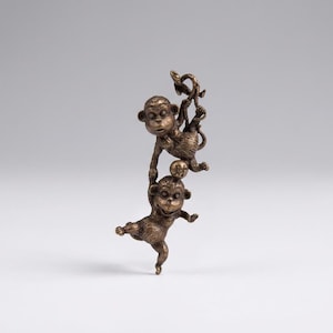 May include: A bronze-colored sculpture of two monkeys. One monkey hangs from a vine, while the other balances on a ball. The sculpture has a detailed texture and is set against a plain background.