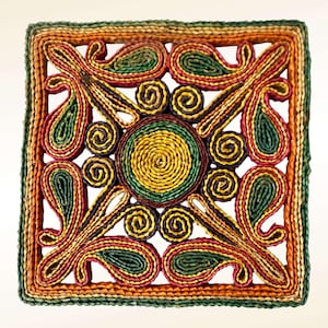 May include: Square woven trivet with a colourful design. The trivet features a central yellow circle surrounded by green, red, and yellow swirls and paisley shapes. The border is a mix of green, orange, and yellow.