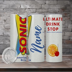 May include: Three white insulated tumblers with various designs. One features the Sonic logo, another has a name in blue script, and the third says "Ultimate Drink Stop" with a fruit graphic. A clear lid sits in front.