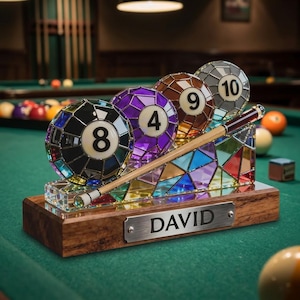 Pode incluir: Um expositor decorativo com quatro bolas de bilhar de vidro colorido numeradas 8, 4, 9 e 10, dispostas numa base de vidro transparente com um taco de bilhar em miniatura. A base assenta num suporte de madeira com uma placa gravada DAVID.