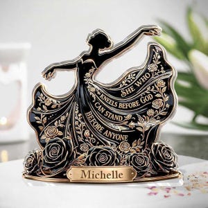 May include: A black and gold figurine of a woman in a flowing dress, with the text "She Who Kneels Before God Can Stand Before Anyone." The base features black roses and a nameplate that reads "Michelle."