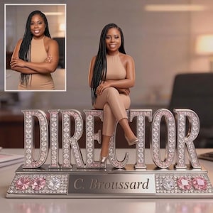 Puede incluir: Una placa de escritorio personalizada con la palabra DIRECTOR en grandes letras plateadas incrustadas con pedrería clara y rosa. Una figura en miniatura de una persona con traje beige se sienta sobre las letras. Una placa indica C. Broussard.