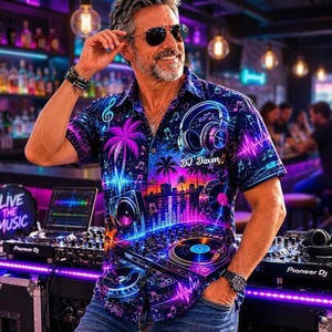 May include: A short-sleeved button-down shirt featuring a vibrant neon graphic print of DJ equipment, headphones, palm trees, and musical notes against a dark blue background. The shirt includes the text DJ Daxen printed on the chest area.